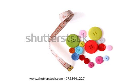 Vertical composition of a white measuring tape next to colorful plastic buttons isolated on a white background.