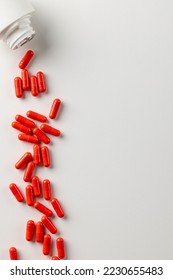 Vertical composition of white pill box spilling red pills on white background with copy space. Medicine, medical services, healthcare and health awareness concept.