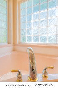 Vertical Corner Bathtub With Deck Mounted Widespread Stainless With Gold Faucet Fixture. Bathtub In A Bathroom Against The Large Windows With Textured Glass Panels.