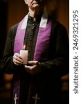 Vertical crop shot of senior Catholic priest wearing soutane and stole holding candle in hands