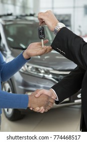 Vertical cropped close up of a car dealer and his client shaking hands. Professional salesman giving car keys to his customer sharing handshake cars on the background buying buyer purchasing renting - Shutterstock ID 774468517