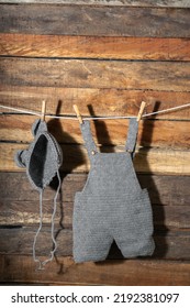 Vertical Detail Shot Of Baby Clothes, Hanging From A Clothesline With Wooden Hooks, Overalls And Hat. Clothes Are Drying In The Shade. Copy Space. Cleaning Concept. Hand Crochet Knitted.