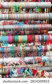 Vertical display stand filled with rows of colorful handmade woven friendship bracelets and thin thread wristbands on a market stall