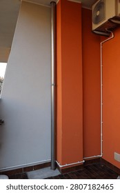 A vertical drainage pipe and a white electrical wire conduit on a minimalist contrast orange and white wall.

