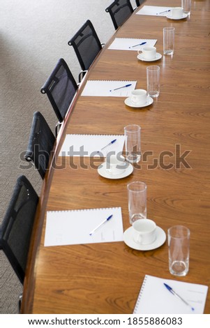 Imagen vertical elevada de una mesa de conferencias vacía con bolígrafos, bolígrafos, vasos y tazas de té en una oficina.