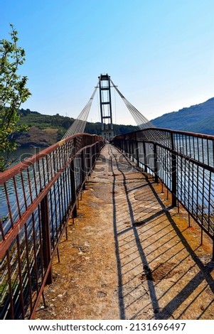 A vertical of an empty suspension bridge with metallic handrails above a seascape and mountains on a sunny day