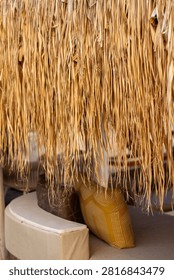 Vertical eye level close up shot of straw thatch fringe hanging from an umbrella canopy above comfortable beach lounge seating with pillows