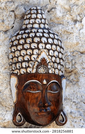 Vertical eye level close up shot of a carved wooden Buddha mask mounted on a rough stone wall