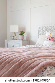 Vertical Feminine Bedroom With Floral Bedsheet And Pink Blanket On The Bed Against Wall. Modern Lampshade And Potted Flowers Are On The Sidetable With Drawers.