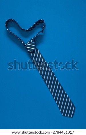 Vertical Flat Lay of Striped Blue Necktie Shaped Like Heart or Mustache on Blue Background. Top View Minimalist Father's Day, Valentine or Birthday Concept Greeting Card Design with Copy Space.