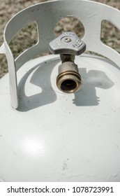 Vertical Frame Of An Angled Overhead Close-up Of The Top Of A White Propane Tank And Brass Valve With Grass In The Background