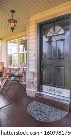 Vertical Frame Home With Chairs On Porch And Brown Door With Glass Panes And Welcome Sign