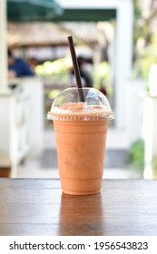 Vertical Front View of Thai Milk Tea Frappe in transparent plastic glass, selective focus on glass with blurred background of balcony.