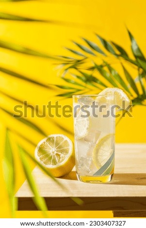 Vertical frontal view of a lemonade glass with ice cubes on a wooden table and palm leaf