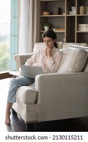 Vertical Full Length Image Concentrated Young Barefoot Hispanic Woman Using Computer, Sitting On Comfortable Couch, Involved In Working On Online Project, Reading News Or Web Surfing Information.