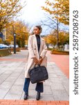 Vertical full length photo of a business style african american model with trench coat and handbag posing outdoors