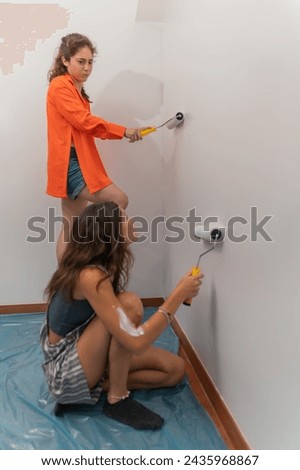 Vertical full length photo of two latin young women redecorating the house painting in white [[stock_photo]] © 