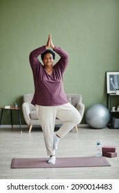 Vertical Full Length Portrait Of Active Senior Woman Doing Yoga At Home And Practicing Balance