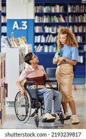 Vertical Full Length Portrait Of Asian Student With Disability Talking To Friend In College Library Setting