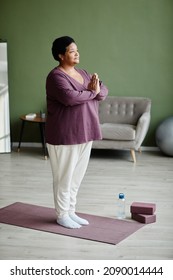 Vertical Full Length Portrait Of Black Senior Woman Meditating At Home In Cozy Interior