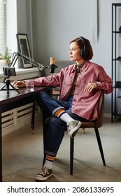 Vertical Full Length Portrait Of Female Content Creator Speaking To Microphone While Recording Podcast In Studio