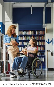 Vertical Full Length Portrait Of Smiling Young Woman With Disability Talking To Friend In College Library