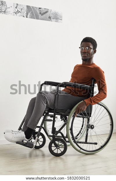 Vertical full length portrait of young\
African-American man using wheelchair and looking at camera while\
exploring modern art gallery\
exhibition