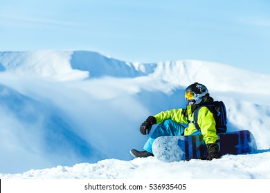 Vertical full length shot of a female snowboarder wearing yellow pants blue jacket yellow helmet and ski goggles posing with her snowboard at the mountains extreme sports recreation free ride concept