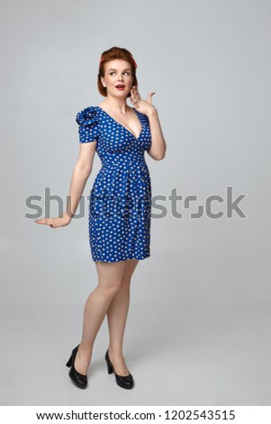 Vertical full length shot of gorgeous elegant young Caucasian female with curvy body and bright make up gesturing excitedly in studio, expressing surprise because of astonishing shocking news