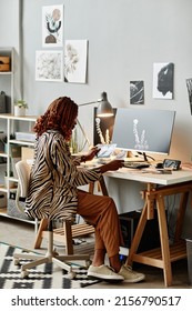 Vertical Full Length Shot Of Young Female Creator At Home Office Workplace With Graphic Prints