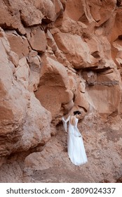 Vertical Full Length View of Boho Bride in Backless Wedding Dress Looking Down by Red Canyon Wall