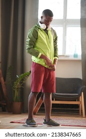 Vertical Full Shot Of Handsome Young African American Man Standing In Living Room At Home Getting Ready For Workout Putting On Sports Clothes