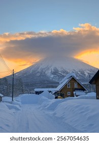 VERTICAL: Glowing orange sunset illuminates Mt. Yotei towering above the wintry wonderland near Niseko, Japan. Idyllic shot of a residential part of the snow-covered countryside near Niseko, Japan.
