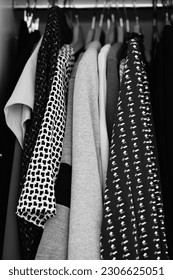 A vertical grayscale closeup of the clothes in a wardrobe.