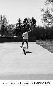 A vertical grayscale shot of a back view of a young man performing a boardslide trick on a skateboard