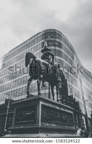 A vertical grayscale shot of Equestrian statue of the Duke of Wellington near an architectural building in Glasgow