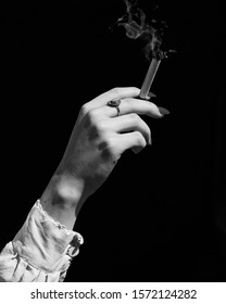 A Vertical Grayscale Shot  Of A Female Hand Holding A Marijuana Blunt On Black Background - Addiction