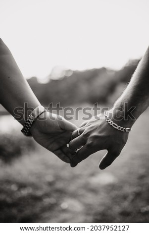 A vertical grayscale shot of a loving couple's hands, outdoors