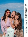 Vertical group of only women taking a selfie portrait on the beach on her summer vacations. Female friends having fun together and enjoying a shore trip. Portrait of three young girls at seaside party