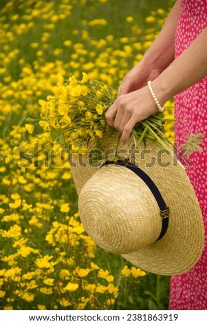 A vertical of a hand holding a bouquet of yellow flowers and a straw hat