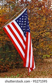 A Vertical Hanging American Flag Outside Against A Fall Background