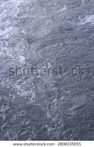 Vertical high angle close-up texture of turbulent river water with white foam and ripples