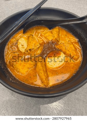 Vertical high angle shot of an authentic Malaysian style curry mee or curry laksa with rich coconut gravy, tofu puffs, fish cakes, and a boiled egg in a black bowl.