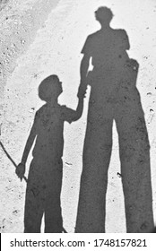 A vertical high angle shot of the shadow of a person holding the hand of a child
