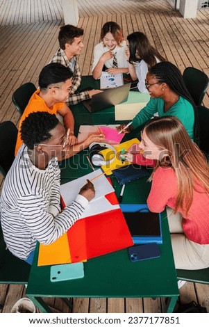 Vertical high angle view of a big group of multiracial teenage students working on university assignment homework project on high school library. Teamwork of diverse young classmates studying together