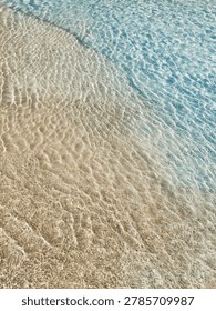 Vertical high angle view of clear transparent ocean water with small ripples over a golden sand beach.
