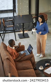 Vertical high angle view at two people chatting in cozy coffee shop enjoying everyday routine