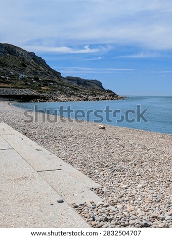 A vertical, high-angle composition showcasing the concrete pedestrian promenade running alongside the vast pebble and shingle shoreline of Chesil Cove