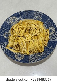 Vertical high-angle shot of sliced thin egg omelette strips served on a classic blue and white patterned porcelain plate.