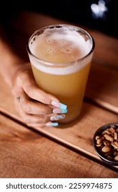 The vertical high-angle view of a hand holding a glass of craft beer on the wooden surface